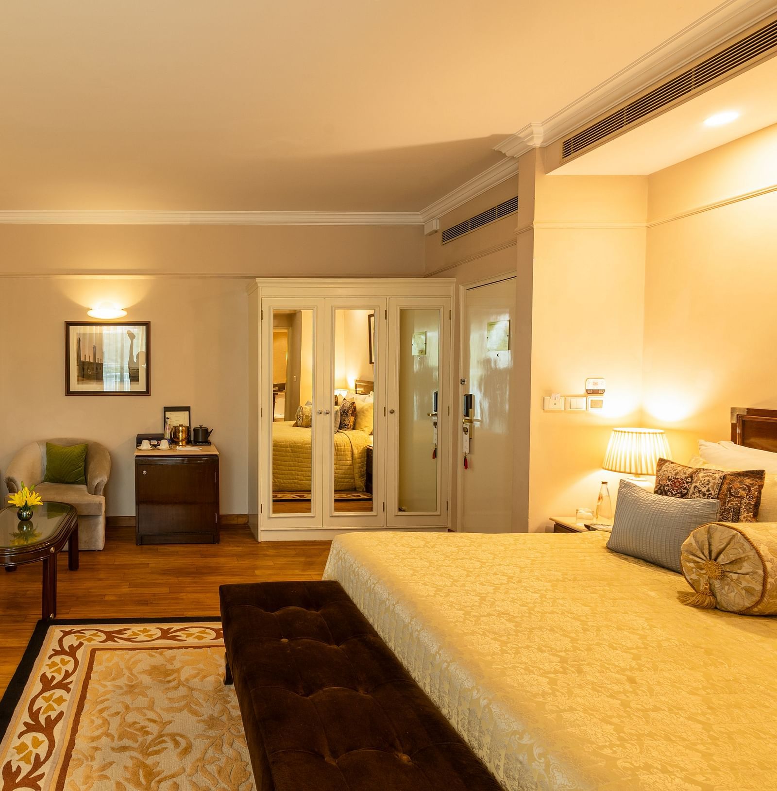 Luxury King Bed Room with Balcony at The Claridges New Delhi, featuring a plush bed, wall-mounted TV, and a cosy sofa in the corner